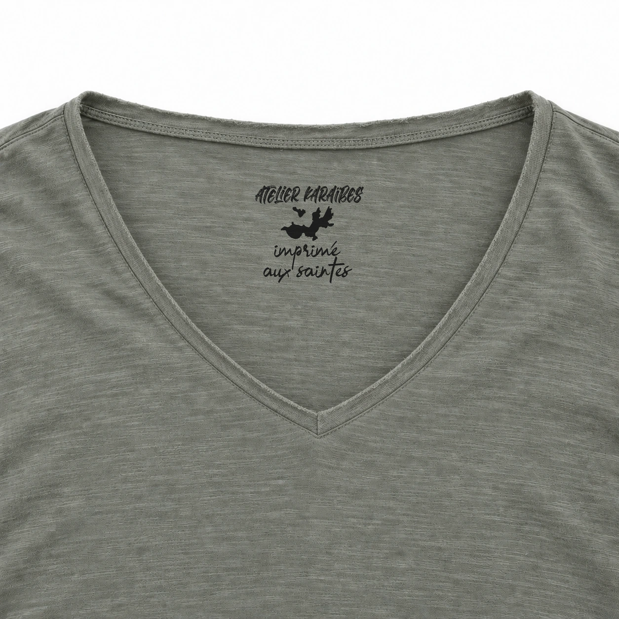 Étiquette intérieure Atelier Karaïbes « imprimé aux Saintes » en noir sur le T-shirt col V Almond Green