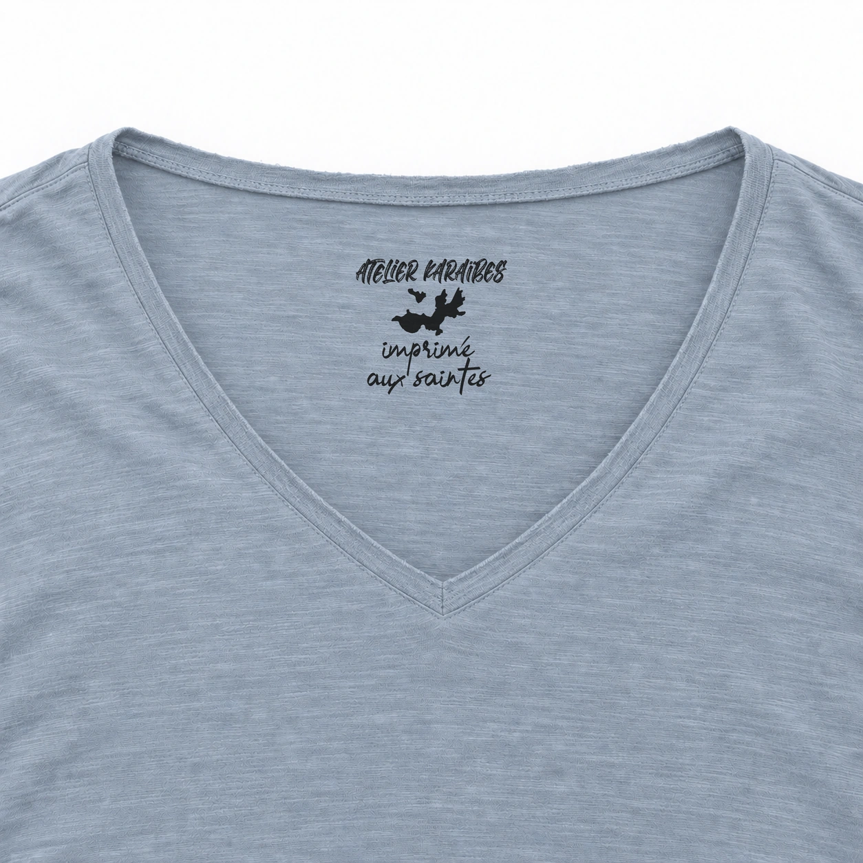 Étiquette intérieure Atelier Karaïbes « imprimé aux Saintes » en noir sur le T-shirt col V Aquamarine