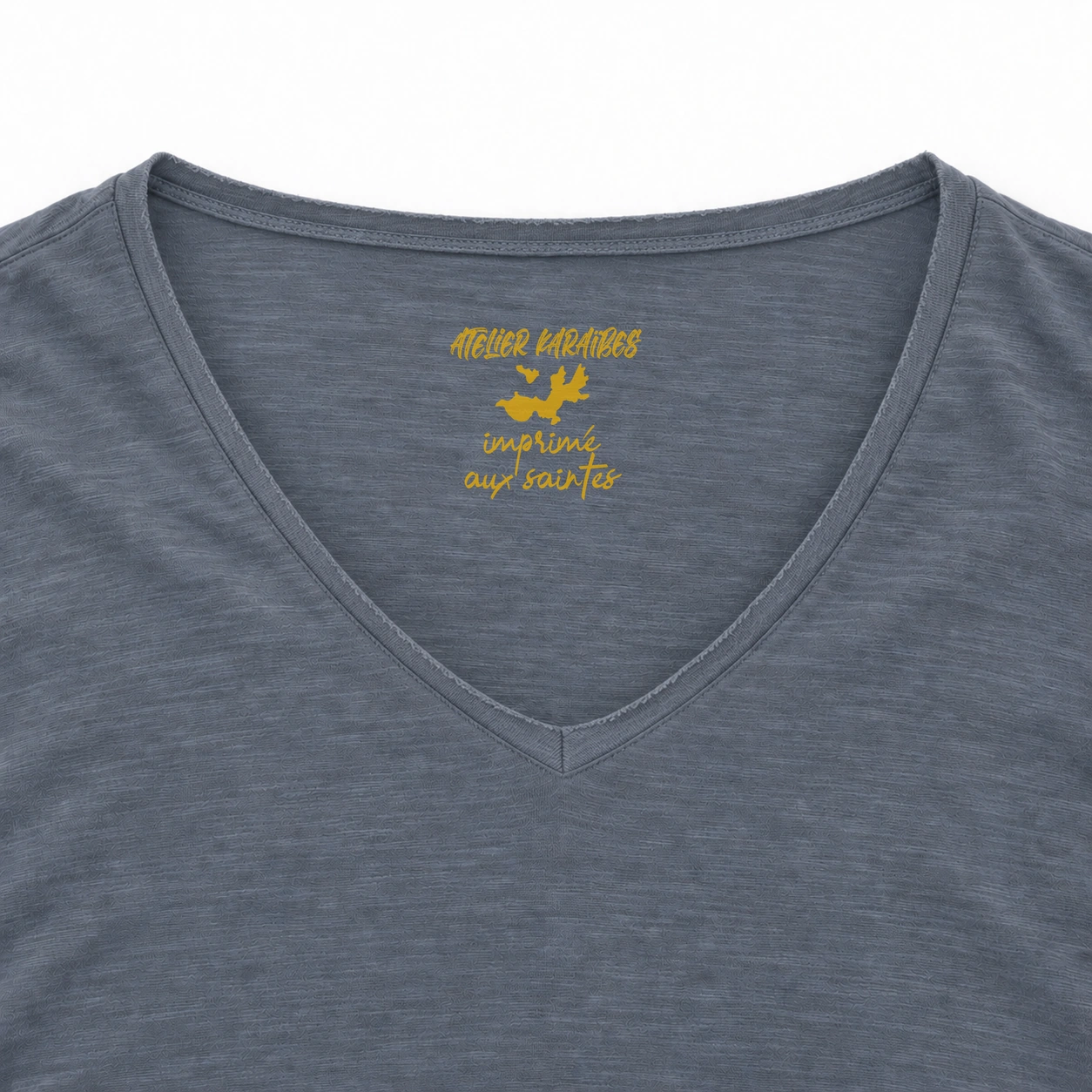 Étiquette intérieure Atelier Karaïbes « imprimé aux Saintes » en jaune moutarde sur le T-shirt col V Mineral Grey