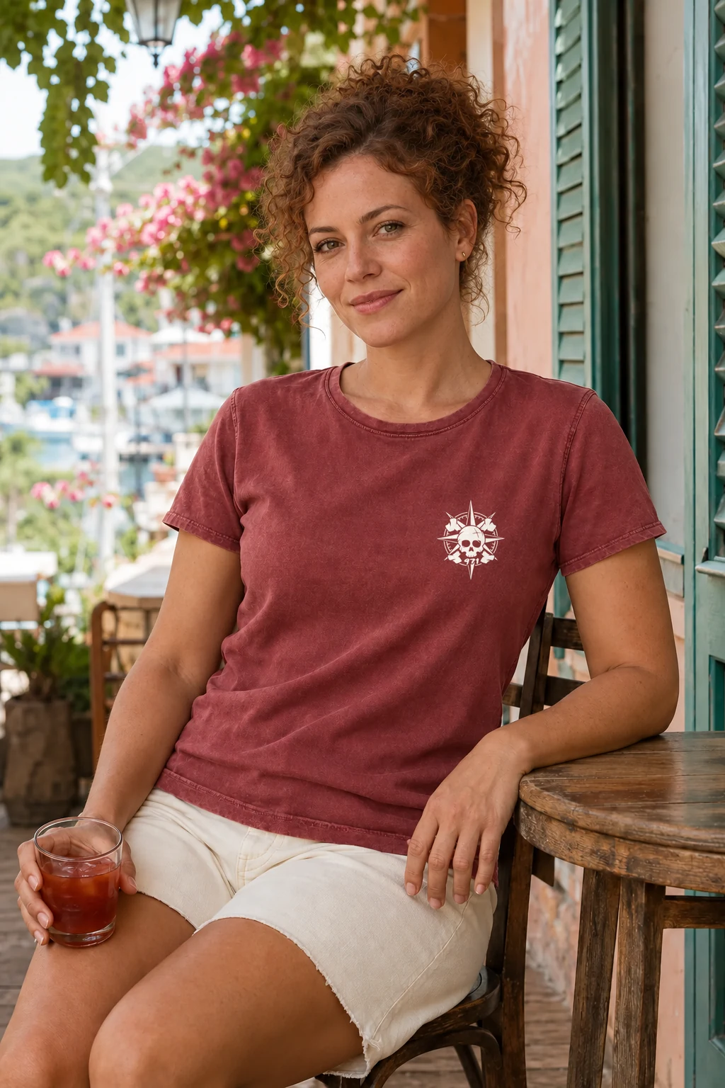 T-shirt vieilli femme rouge grenat délavé avec une boussole pirate 971 ornée d’un crâne imprimé en blanc, porté par une femme à la terrasse d’un café créole aux Saintes