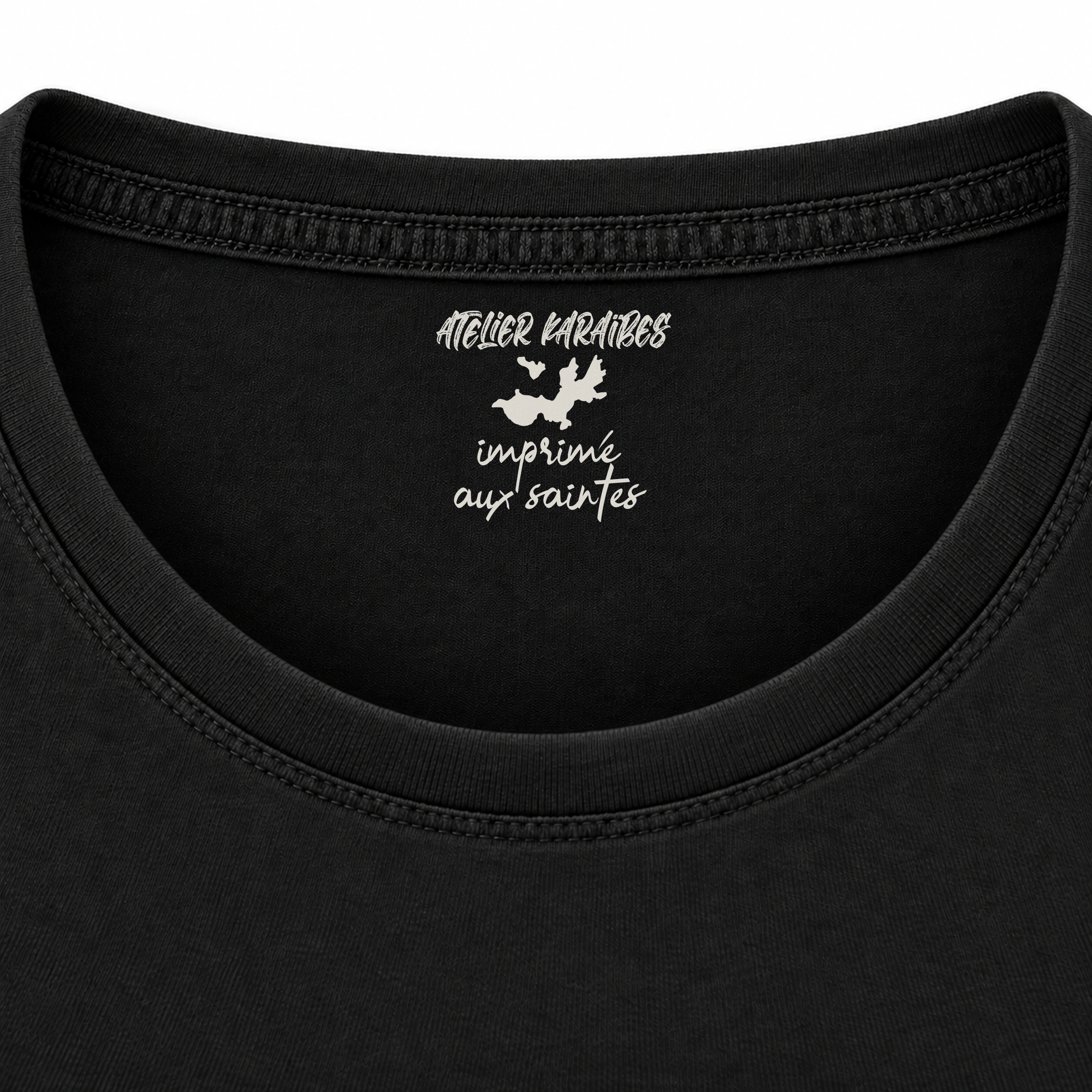 Étiquette intérieure Atelier Karaïbes « imprimé aux Saintes » en blanc sur le T-shirt rouloté noir
