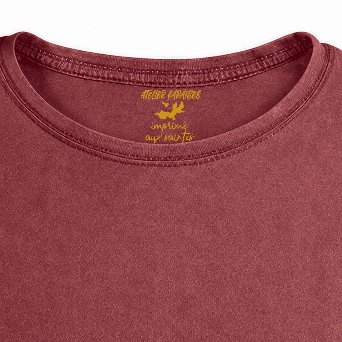 Gros plan de la signature intérieure Atelier Karaïbes imprimée en jaune moutarde sous le col du T-shirt vieilli homme rouge grenat délavé